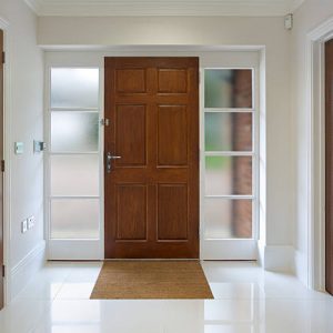 a front door of a new house with a high quality large oak panelled front door set in a white frame with opaque glass windows on either side. To the left is a door to a cloak cupboard and to the right is a glass panelled door to a reception room.