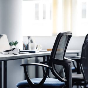 Modern gadgets in interior of coworking office during COVID-19 epidemic. Chairs and desk for support workers, laptops and headphones, cups and stationery in daylight on window background, free space